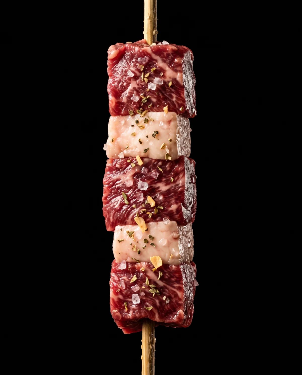 Detalhe de um espetinho bovino cru, temperado com sal grosso e ervas